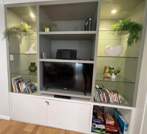 a white entertainment center with a tv and books at The Sandy Villa 150 meters from Sawtell Beach in Sawtell