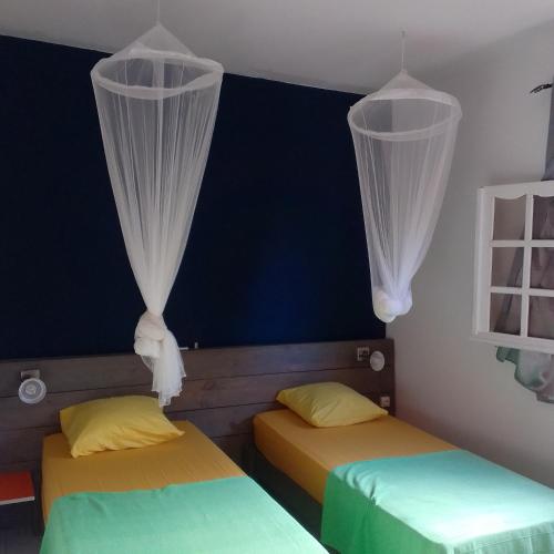 two beds in a room with white curtains at Maison de campagne proche des plages in Sainte-Rose