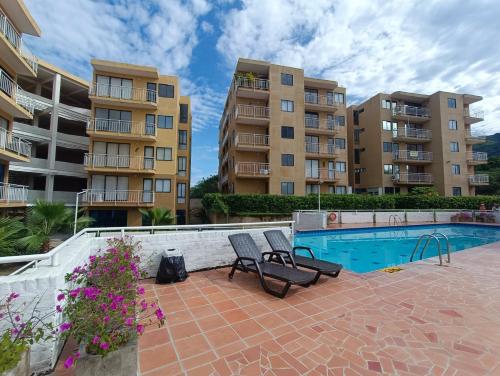 una piscina con 2 sillas y 2 edificios en Apartamento Portal de la Sierra 3 Habitaciones, en Santa Marta