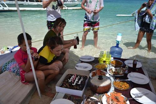 a group of people sitting around a table with food on the beach at Jao bay boat charter in Talibon