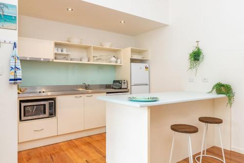 a kitchen with white cabinets and a counter and stools at Mobys Resort 35 in Boomerang Beach
