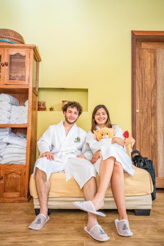 a man and woman sitting on a bed with a teddy bear at El Jardin Lodge & Spa in Puerto Misahuallí