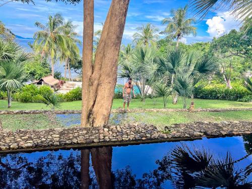 a man standing next to a body of water with palm trees at The Dream Beach Resort in Taytay
