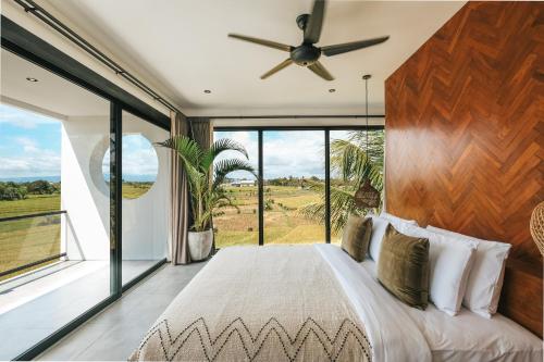 um quarto com uma cama grande e janelas grandes em Botanique Villa & Studio em Tanah Lot