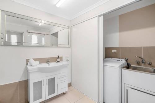 a white bathroom with a sink and a washing machine at Inner City Serenity in Cairns