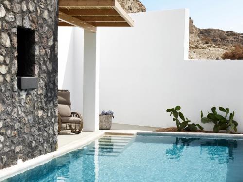 a swimming pool in a house with a stone wall at Santo Pure Oia Suites & Villas in Oia