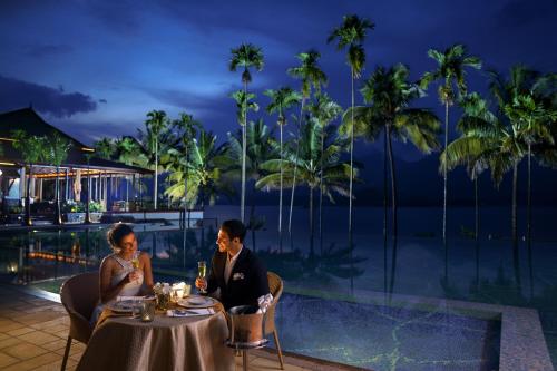 a man and a woman sitting at a table in front of a pool at Taj Wayanad Resort & Spa, Kerala in Wayanad