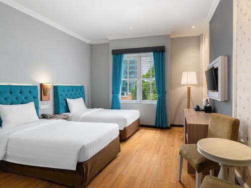 a hotel room with two beds and a table at Luminor Hotel Palembang by WH in Palembang