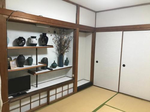 Habitación con estanterías con jarrones y TV. en Ibusiki Shizuka en Ibusuki