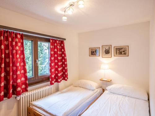 2 Betten in einem Zimmer mit roten Vorhängen und einem Fenster in der Unterkunft Apartment Chesa Mulin by Interhome in Celerina
