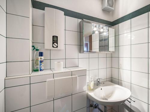 a white tiled bathroom with a sink and a mirror at Apartment Point-1 by Interhome in Maishofen