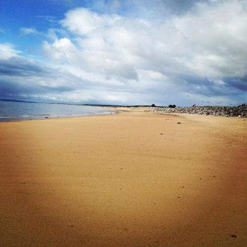 a sandy beach with the ocean on a cloudy day at Frasers Apartment in Golspie