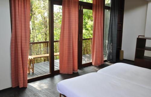 a bedroom with a bed and a balcony with sliding glass doors at Uravu Bamboo Grove Resort in Wayanad