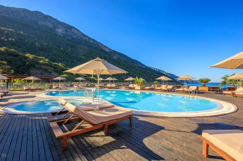 a swimming pool with chairs and umbrellas and a mountain at Manaspark Deluxe Hotel in Oludeniz