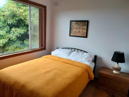 a bedroom with a bed with a yellow blanket and a window at Seahaven in Lake Tyers