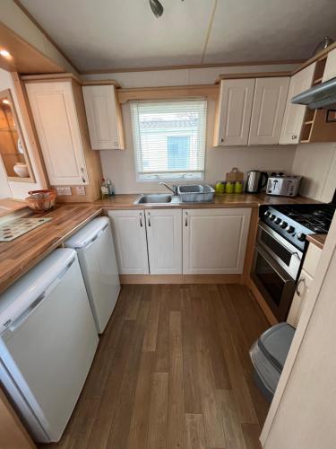 a small kitchen with white cabinets and wooden floors at Bittern 8, Scratby - California Cliffs, Parkdean, sleeps 8, free Wi-Fi, pet friendly - 2 minutes from the beach! in Scratby