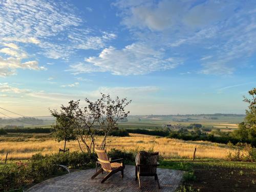 2 chaises assises sur une terrasse avec vue sur un champ dans l'établissement The Shepherds Farm, à Heuvelland