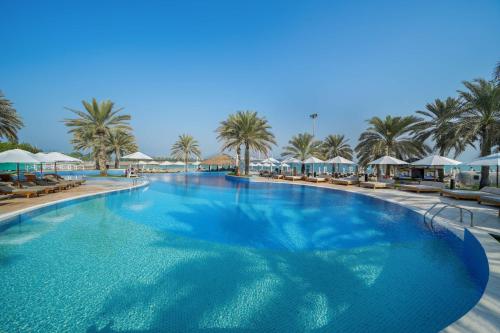 a large swimming pool with palm trees and umbrellas at Radisson Blu Hotel & Resort, Abu Dhabi Corniche in Abu Dhabi