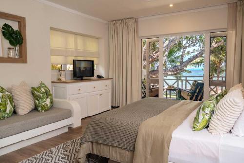een slaapkamer met een bed, een tv en een balkon bij Indian Ocean Lodge in Grand'Anse Praslin