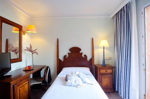 a bedroom with a bed and a desk and a television at Hotel Cala Sant Vicenç - Adults Only in Cala de Sant Vicent