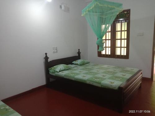 a bedroom with a bed with a green comforter and a window at Ancient Tree in Mirissa