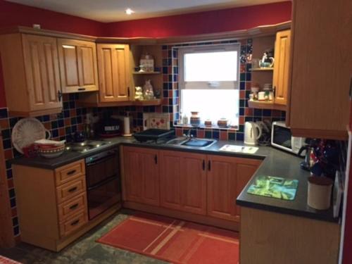 una cocina con armarios de madera y una ventana en Primrose Cottage, Bushmills - Cosy Self Catering Property, en Bushmills