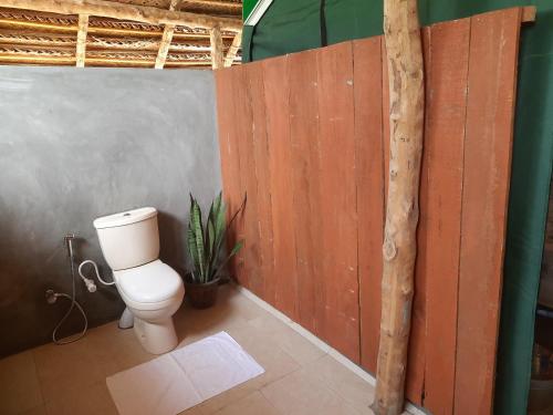 a bathroom with a toilet and a wooden wall at Nirvaan Safari Lodge in Wilpattu