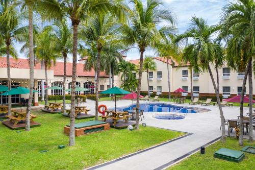 a resort with a pool and tables and palm trees at Quality Hotel Real Aeropuerto San Salvador in San Luis