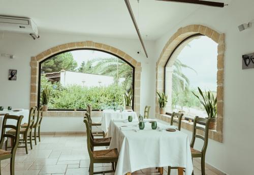 restauracja z białymi stołami i krzesłami oraz dużym oknem w obiekcie Oppure - Masseria Moderna w mieście Polignano a Mare