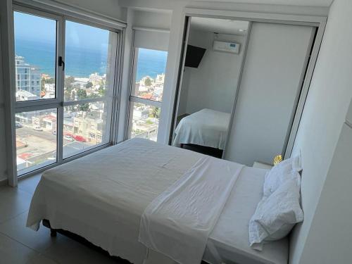 a bedroom with a white bed and large windows at Moderno Depto con Vista al Mar in Comodoro Rivadavia