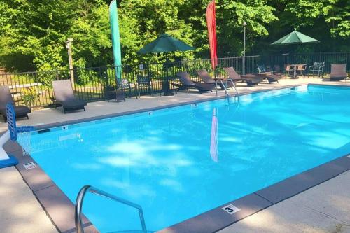 a large blue swimming pool with chairs and umbrellas at Cabin Coco - June sale dates! Luxe A Frame with projector screen, arcade and swim spa in Sevierville