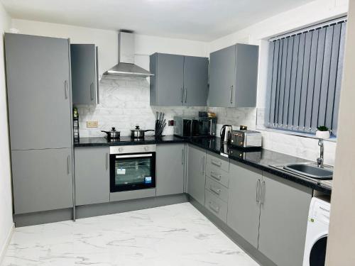 uma cozinha com armários cinzentos e brancos e um lavatório em Beautiful and Homely 3 Bed House With FREE Parking So Close To Man City and City Centre em Manchester