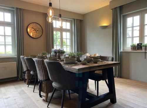 a dining room table with chairs and a clock on the wall at Sfeervol familielandhuis in de groene Kempen in Baarle-Hertog