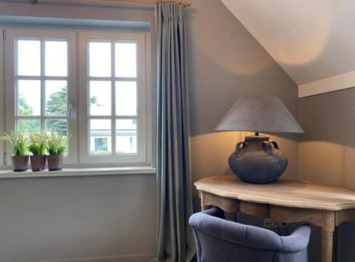 a lamp on a wooden table next to a window at Sfeervol familielandhuis in de groene Kempen in Baarle-Hertog