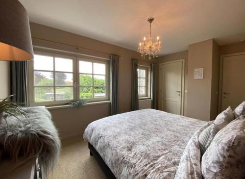 a bedroom with a bed and windows and a chandelier at Sfeervol familielandhuis in de groene Kempen in Baarle-Hertog