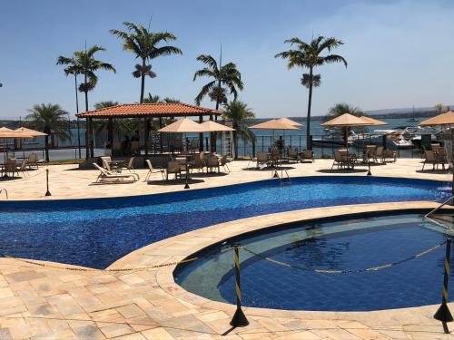a swimming pool with tables and chairs and palm trees at Flat Decoração Náutica c/Vista Lago Paranoá in Brasilia