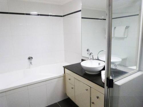 a white bathroom with a sink and a bath tub at Ultra Convenient Apartment HER09029 in Sydney