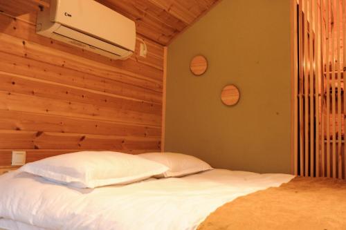 1 dormitorio con cama blanca y pared de madera en Jvarisa Glamping, en Ambrolauri