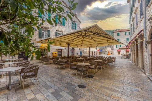 a patio with tables and chairs and a large umbrella at Hotel Vardar in Kotor