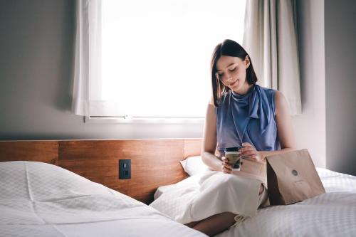 a woman sitting on a bed holding a drink at EN HOTEL Kyoto in Kyoto