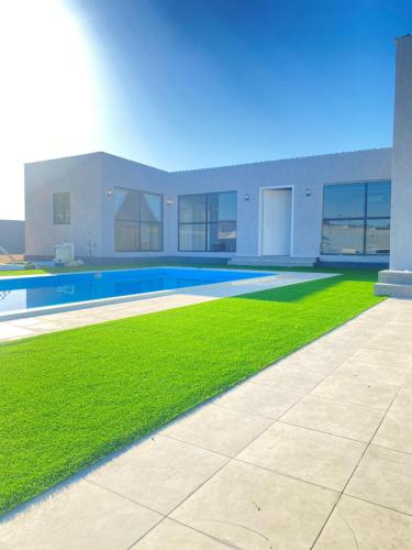 un patio con piscina y césped verde en شاليه ريفان, en Umm Lajj