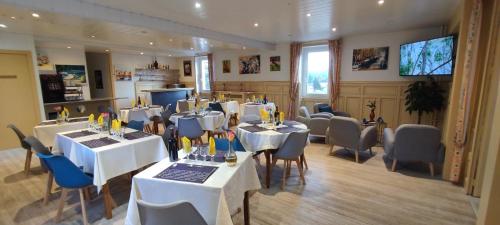 un ristorante con tavoli e sedie bianchi e una televisione di Hotel Belle Vue a Souillac