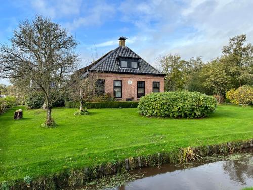 a brick house on a grassy yard next to a river at Het Wylde Pad - Let’s go Wylde! in Twijzelerheide
