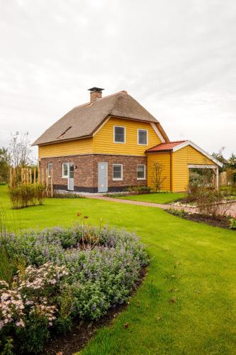 a large yellow house with a yard with flowers at Waterresort Bodelaeke Giethoorn in Giethoorn