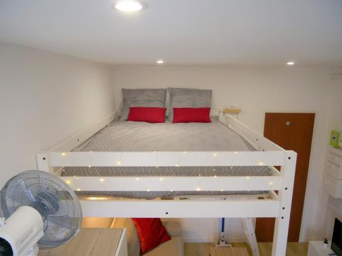 een wit bed met 2 rode kussens en een ventilator bij Studio Northwich centre-ville in Dole