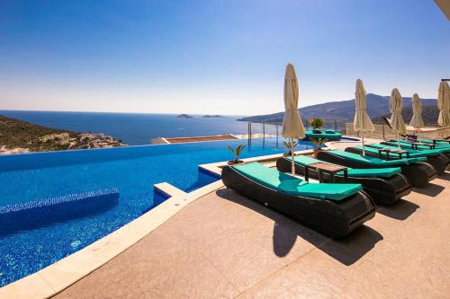 einen Pool mit Liegestühlen, Sonnenschirmen und dem Meer in der Unterkunft Villa Pırlanta, Kalkanvilla in Kalkan