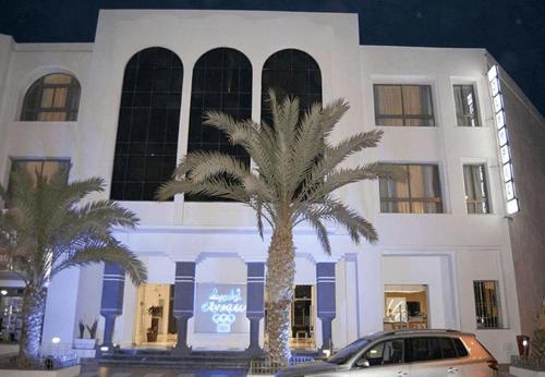 um carro estacionado em frente a um edifício com uma palmeira em HOTEL OLYMPIC DJERBA em Djerba
