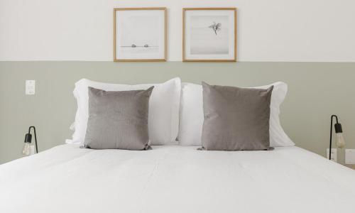 a white bed with pillows and two pictures on the wall at Tabas Espaçoso apê no Jardim Botânico JB0003 in Rio de Janeiro