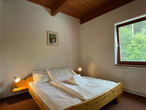 a bedroom with a bed with white sheets and a window at Apartmány Doky Holiday in Lipno nad Vltavou
