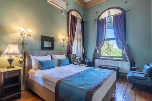 a bedroom with a bed and a chair and two windows at Büyükada Anastasia Meziki History Mansion in Buyukada